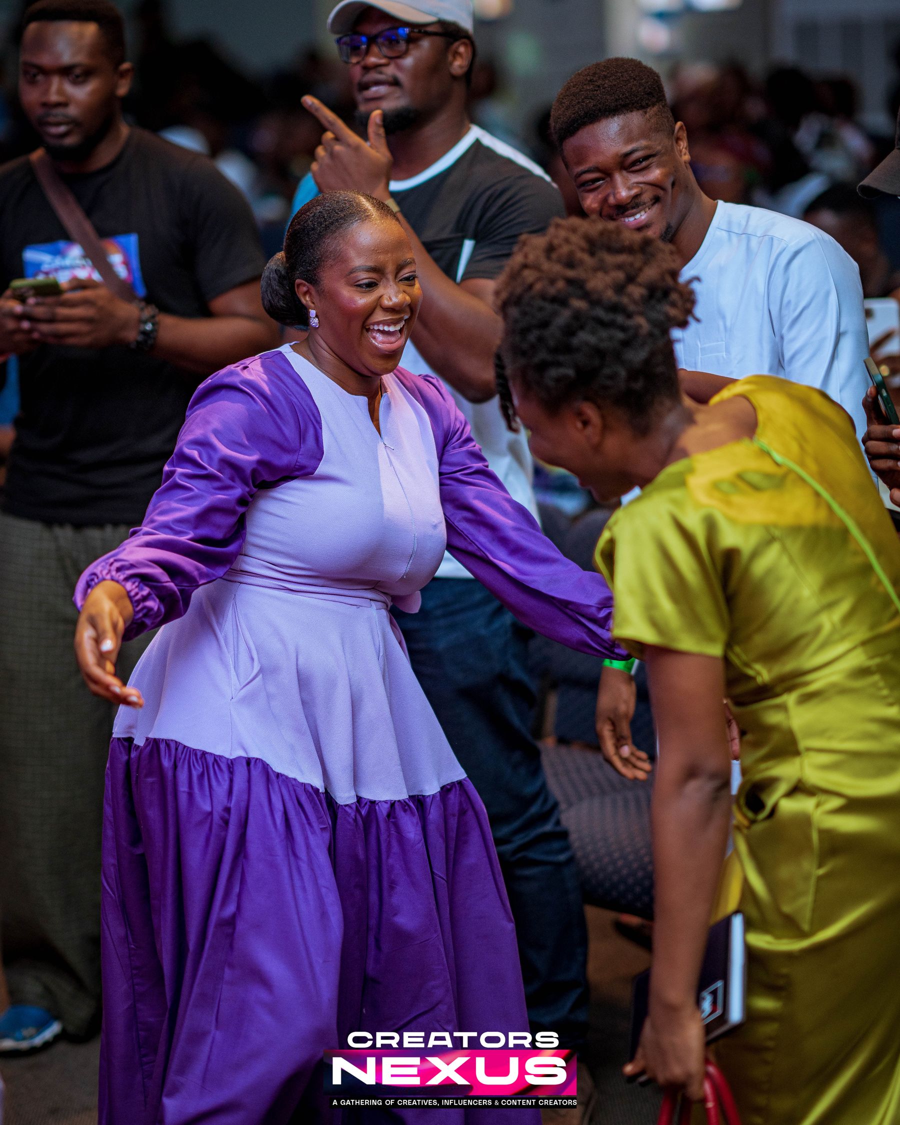Two attendees greeting each other, laughing, in the crowd at a Creators Nexus conference.